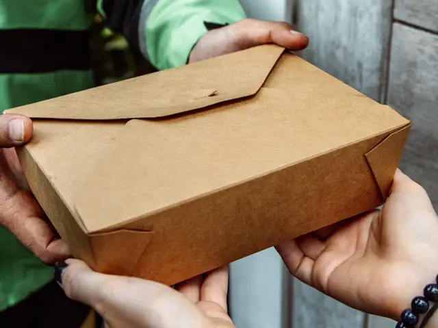 Two people's hands exchanging brown box of takeout food